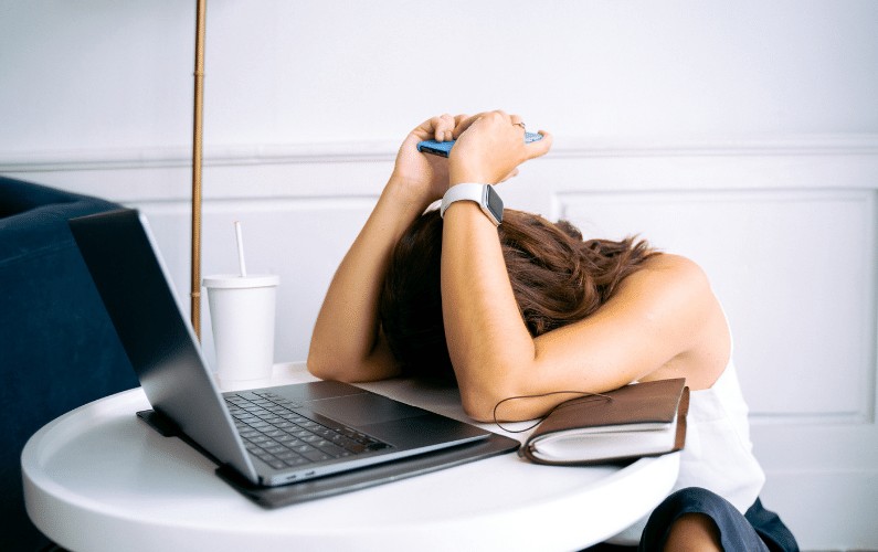 Girl sitting with her head her desk and her laptop in front of her.